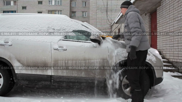 Водитель очищает автомобиль от снега во время прогрева двигателя, зима. Стоковое видео, видеограф Кекяляйнен Андрей / Фотобанк Лори