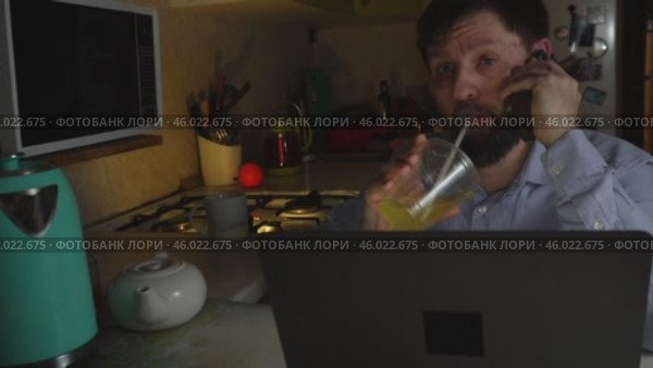 Взрослый мужчина, поздно вечером работающий на кухне за ноутбуком, отвечает на телефонный звонок. Стоковое видео, видеограф Ярославский Максим / Фотобанк Лори