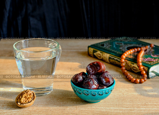 Walnut, turquoise piala with dates, glass of clear water, rosary and book of Quran on table First meal, Muslim fast Eid al, Uraza. Стоковое фото, фотограф Ирина Кононова / Фотобанк Лори