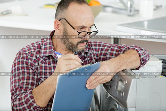 washing machine serviceman looking over top of glasses to write. Стоковое фото, агентство Ingram Publishing / Фотобанк Лори