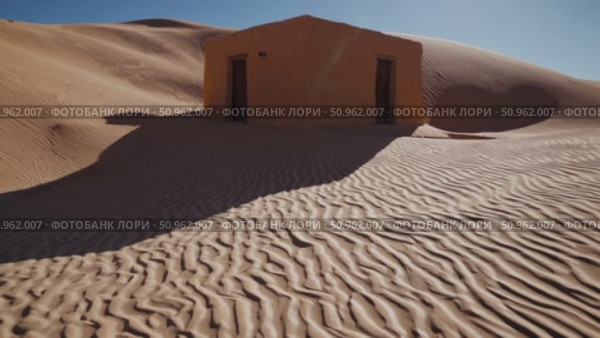 Weathered orange structure standing amid rippling desert sand, casting dramatic shadows against cloudless azure sky, emphasizing architectural decay within expansive arid terrain. Стоковое AI-видео, аниматор Данил Руденко / Фотобанк Лори
