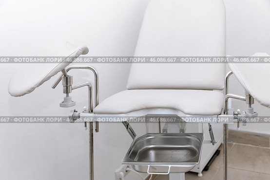 White modern gynecological examination chair for women. Medical chair in the gynecologist's office with white wall. Reproductive system and Pregnancy concept. High quality photo. Copy space. Стоковое фото, фотограф Ирина Михайличенко / Фотобанк Лори