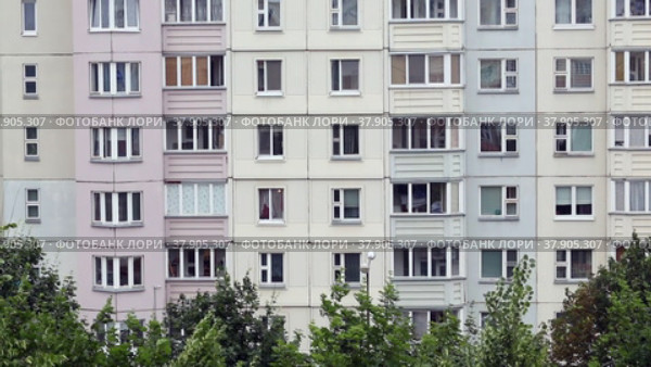 Windows of a multi-storey panel building. At the bottom of the frame, the tops of the trees swaying in the wind. (2022 год). Стоковое видео, видеограф Vadzim Yakubovich / Фотобанк Лори