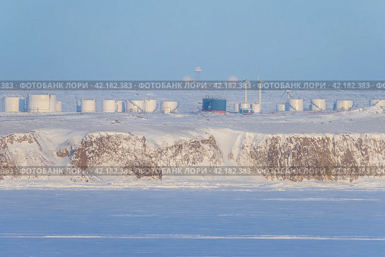 Winter arctic industrial landscape. View of wind turbines and tanks for fuel and oil products on a high rocky shore. Energy and Industry in the Far North of Russia. Chukotka, Siberia, Russian Far East. Стоковое фото, фотограф Андрей Степанов / Фотобанк Лори