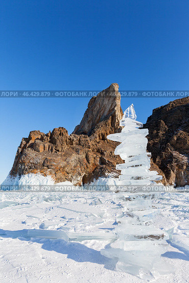 Winter landscape of frozen Baikal Lake in February sunny day. High ice pyramid made of transparent ice floes against backdrop of famous Cape Khoboy - natural landmark of Olkhon Island. Winter travels. Стоковое фото, фотограф Виктория Катьянова / Фотобанк Лори