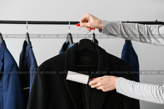 Woman cleaning jacket with lint roller on light background. Стоковое фото, фотограф Pixel_shot / Фотобанк Лори