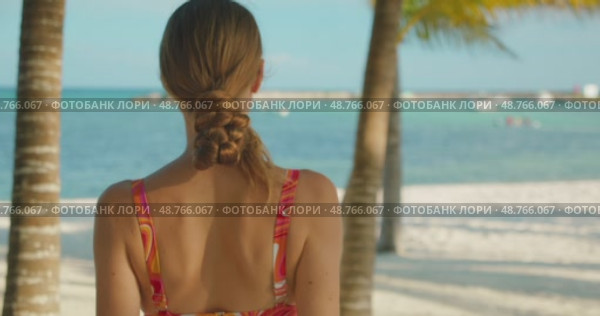 Woman faces sea while walking on sandy beach under palm trees in summer. Стоковое видео, видеограф Ольга Сухарева / Фотобанк Лори