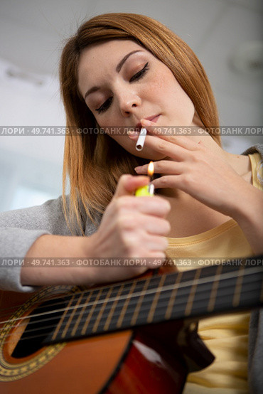 woman guitarist smoking cigarette at home. Стоковое фото, агентство Ingram Publishing / Фотобанк Лори