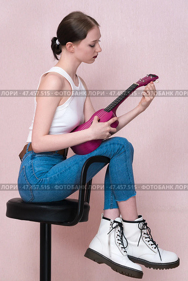 Woman holding ukulele and tuning strings of her musical instrument with concentration. Profile view. Стоковое фото, фотограф А. А. Пирагис / Фотобанк Лори