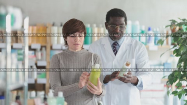 Woman in pharmacy shooses antidandruff shampoo. African man pharmacist in background. Стоковое видео, видеограф Яков Филимонов / Фотобанк Лори