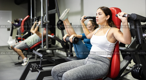 Woman is engaged in sports sitting on simulator in the gym. Woman strengthens muscles of hands on simulator. Стоковое фото, фотограф Яков Филимонов / Фотобанк Лори
