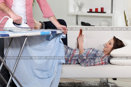 Woman lying on the couch reading while her boyfriend does the housework. Стоковое фото, агентство Ingram Publishing / Фотобанк Лори