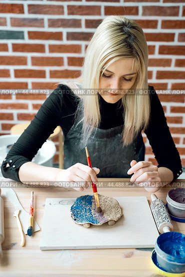 Woman making pattern on ceramic plate with paint brush. Creative hobby concept. Earn extra money, side hustle, turning hobbies into cash, passion into job, vertical. Стоковое фото, фотограф Natalia Gdovskaia / Фотобанк Лори