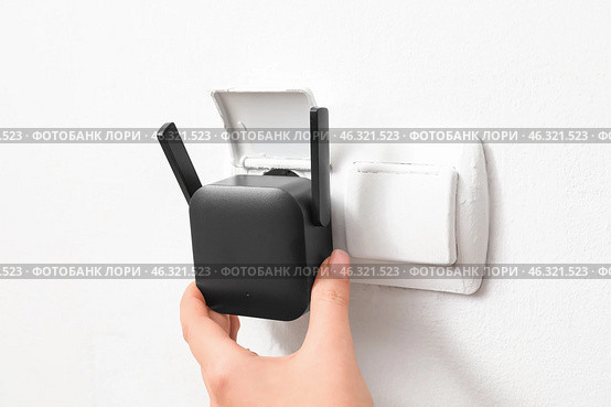 Woman plugging black WiFi repeater in electric socket on white wall. Стоковое фото, фотограф Pixel_shot / Фотобанк Лори