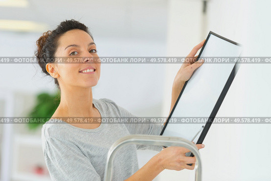 woman positioning picture frame on wall. Стоковое фото, агентство Ingram Publishing / Фотобанк Лори