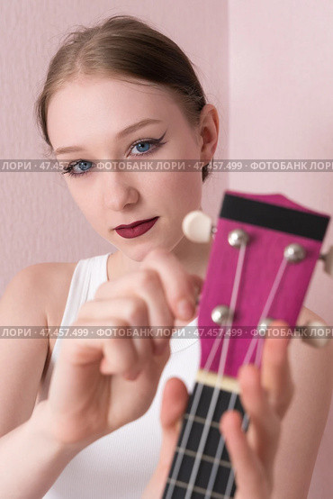 Woman preparing ukulele for use, looking at camera, tightening and loosening strings before playing. Стоковое фото, фотограф А. А. Пирагис / Фотобанк Лори