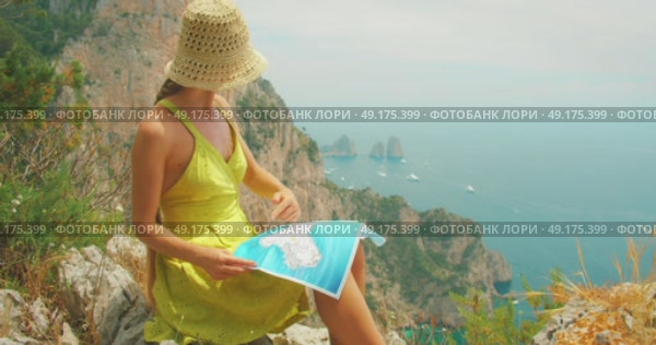 Woman reads map and points toward Faraglioni cliffs and sea in summer Capri, Italy. Стоковое видео, видеограф Igor Tichonow / Фотобанк Лори