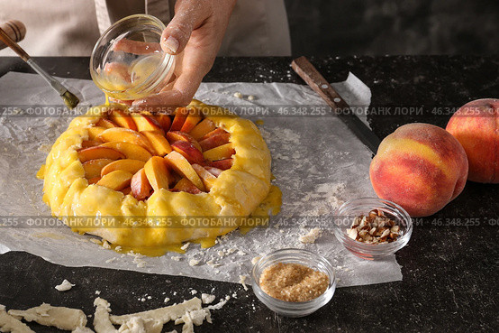 Woman smearing raw peach galette with egg yolk at table. Стоковое фото, фотограф Pixel_shot / Фотобанк Лори
