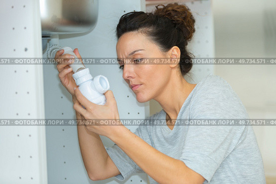 woman tightening pipe under sink with worktool at home. Стоковое фото, агентство Ingram Publishing / Фотобанк Лори
