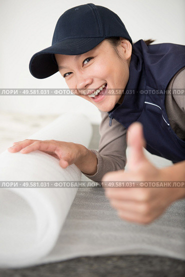 woman unrolling underlay over floor surface. Стоковое фото, агентство Ingram Publishing / Фотобанк Лори