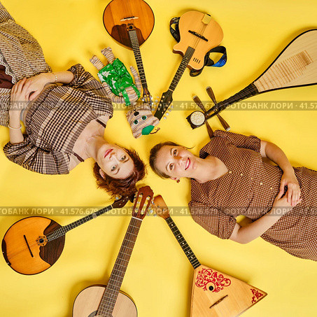 Women musicians in dresses with musical instruments on a yellow studio background. Happy artists with stringed musical instruments with smiles on faces. Стоковое фото, фотограф Андрей Журавлев / Фотобанк Лори