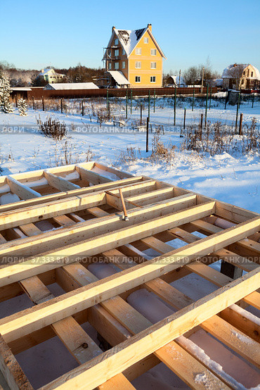 Wood frame house subfloor on pile foundation, real estate under construction against brick house at winter season, Russia. Стоковое фото, фотограф Кекяляйнен Андрей / Фотобанк Лори