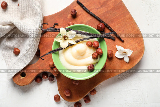 Wooden board with ramekin of tasty vanilla pudding and hazelnuts on light background, closeup. Стоковое фото, фотограф Pixel_shot / Фотобанк Лори