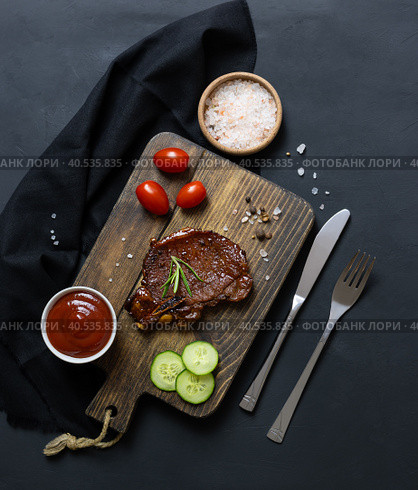Wooden plank with pork steak and vegetables on a black table. Стоковое фото, фотограф Анна Никитина / Фотобанк Лори