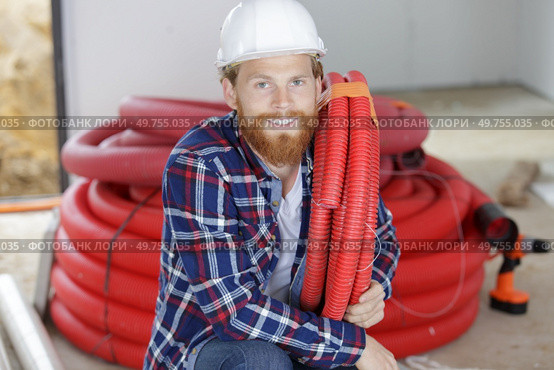 workman crouching down holding red pipe. Стоковое фото, агентство Ingram Publishing / Фотобанк Лори