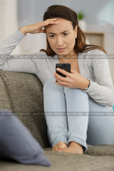 worried lady on sofa in front of smartphone. Стоковое фото, агентство Ingram Publishing / Фотобанк Лори