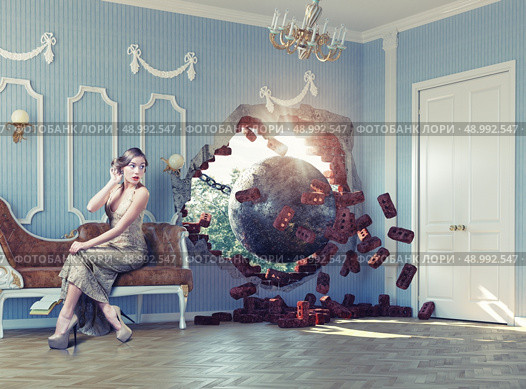 wrecking ball enters the room, scaring the woman on the sofa. Photo combination creative concept. Стоковое фото, агентство Ingram Publishing / Фотобанк Лори