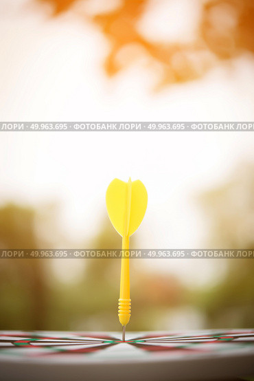 Yellow dart arrow hitting in the center of dartboard. Стоковое фото, агентство Ingram Publishing / Фотобанк Лори