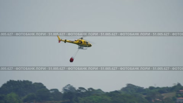 Yellow firefighting helicopter with water bucket. Стоковое видео, видеограф Данил Руденко / Фотобанк Лори