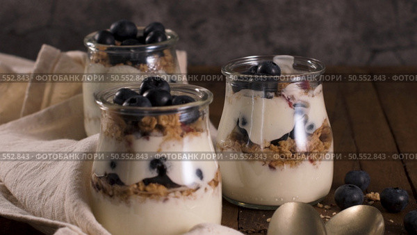 Yogurt parfait with blueberry and granola. Healthy breakfast concept served in mason jar with decorative spoons on wooden table. Стоковое фото, агентство Ingram Publishing / Фотобанк Лори