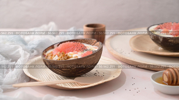 Yogurt with grapefruit, granola, chia and honey served in half a coconut shell on a rose marble kitchen countertop. Стоковое фото, агентство Ingram Publishing / Фотобанк Лори
