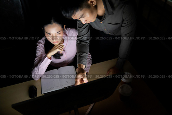 Young adult asian businessman dicuss with collegue about work late at night in their office with desktop computer. Using as hard working and working late concept. Стоковое фото, агентство Ingram Publishing / Фотобанк Лори