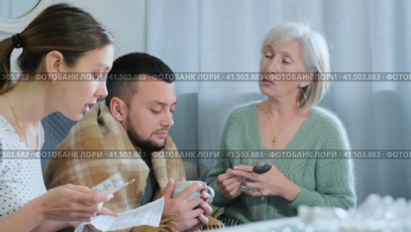 Young adult man having viral disease, elderly mother giving him drugs while his wife reading medicines instruction. Стоковое видео, видеограф Яков Филимонов / Фотобанк Лори