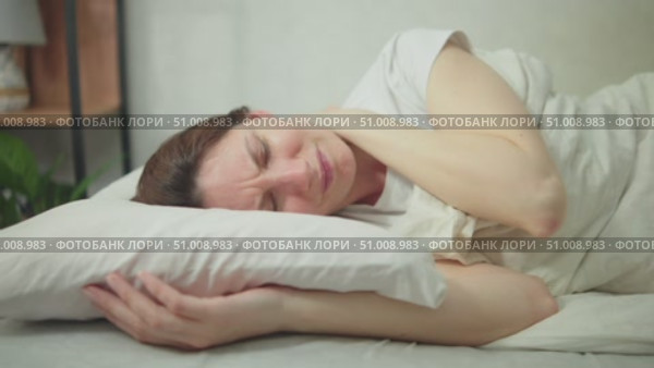 Young adult woman wakes up in the morning in bed and suffers from neck pain. Concept of problems with the spine due to improperly fitted pillow. Стоковое видео, видеограф Денис Кебедов / Фотобанк Лори