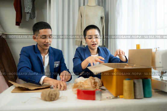 Young Asian businessman and woman Clothes are being packaged for delivery to customers in cardboard boxes and cushioned lump from natural materials that are not toxic to the planet. Стоковое фото, агентство Ingram Publishing / Фотобанк Лори