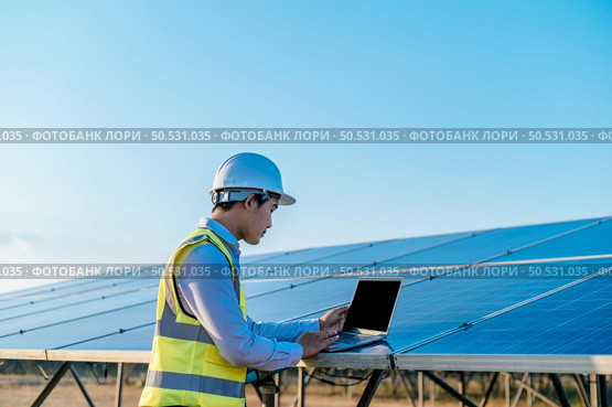 Young Asian technician man checking operation of sun and cleanliness of photovoltaic solar panel and typing on laptop computer while working in solar farm. Стоковое фото, агентство Ingram Publishing / Фотобанк Лори