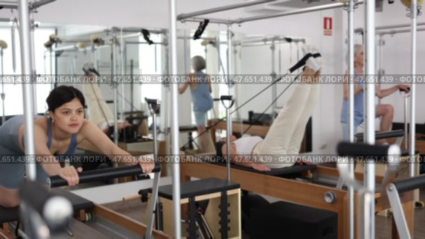 Young asian woman doing stretching exercises on Pilates reformer as part of injury rehabilitation course in modern fitness center. Стоковое видео, видеограф Яков Филимонов / Фотобанк Лори