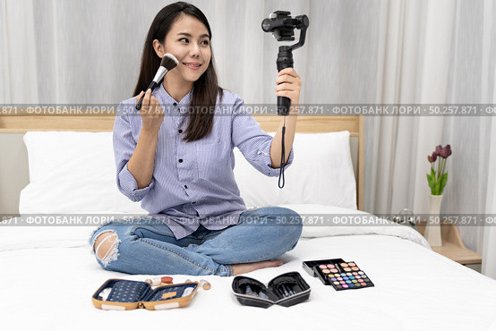 Young beautiful Asian woman beauty vlogger blogger recording live how to make up tutorial to share on social media using Gimbal Stabilizer on mobile phone. Use for vlog social media influencer concept. Стоковое фото, агентство Ingram Publishing / Фотобанк Лори