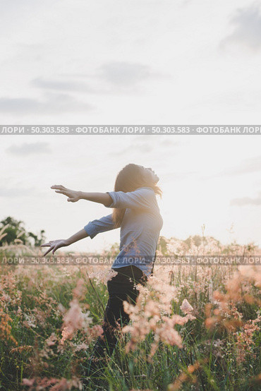 Young beautiful woman standing stretch her arms in the air on the grass field. Woman enjoy with nature during sunset. Стоковое фото, агентство Ingram Publishing / Фотобанк Лори