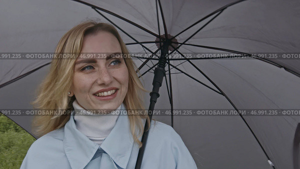 Young blond woman holding grey umbrella outdoors on green meadow. Стоковое фото, фотограф David Kashakhi / Фотобанк Лори