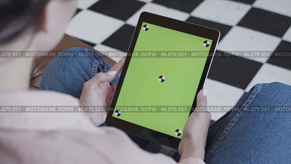 Young brunette woman watching her tablet with green screen on black and white floor background. Стоковое фото, фотограф David Kashakhi / Фотобанк Лори
