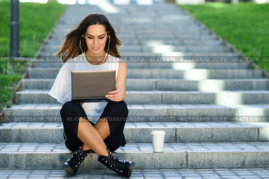 Young businesswoman having a videoconference with her laptop computer sitting on urban steps outdoors.. Middle-age businesswoman working with her laptop computer sitting on the floor. Стоковое фото, агентство Ingram Publishing / Фотобанк Лори