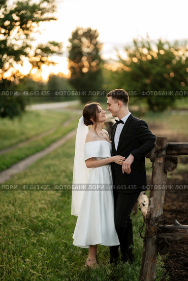young couple the groom in a black suit and the bride in a white short dress on a walk in the village. Стоковое фото, агентство Ingram Publishing / Фотобанк Лори