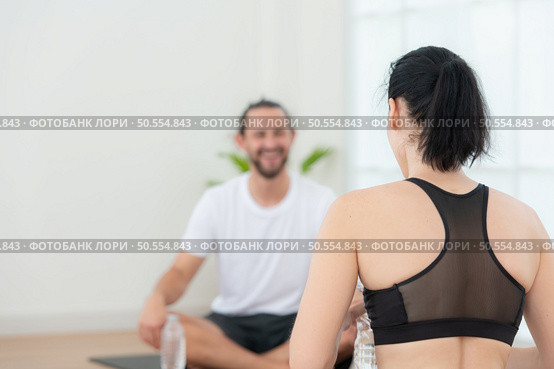 Young female and male athletes sitting rest on yoga mats and drinking water. They are looking at each other and smiling. Стоковое фото, агентство Ingram Publishing / Фотобанк Лори