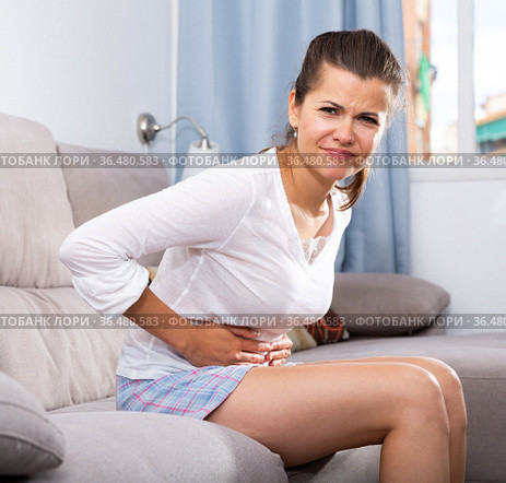 Young female at sofa holding hands on the illness stomache. Стоковое фото, фотограф Яков Филимонов / Фотобанк Лори