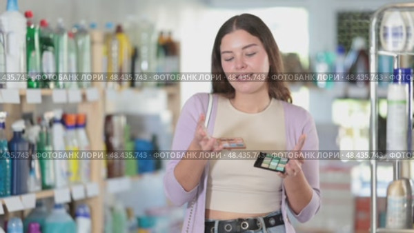 Young female customer choosing cosmetics, looking for lipstick and choosing from several samples in cosmetics shop. Стоковое видео, видеограф Яков Филимонов / Фотобанк Лори